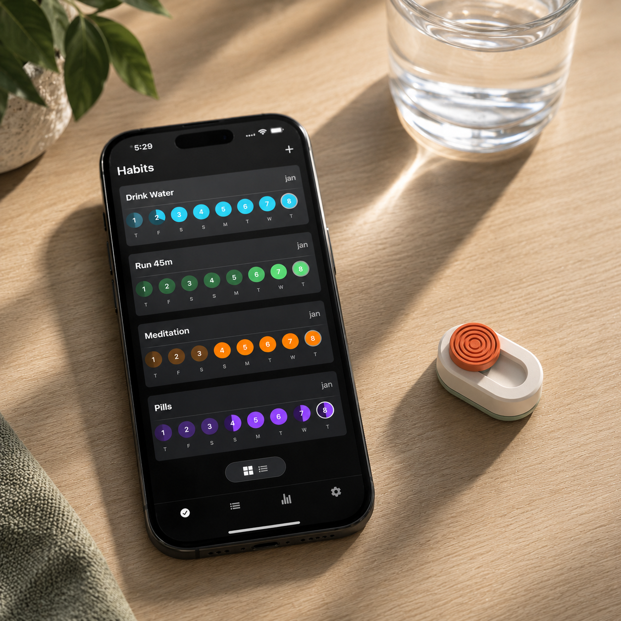 KLIK on a desk beside a phone showing the habit-tracking app